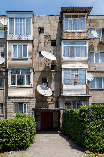 soviet five-storey apartment building with numerous windows and balcony and satellite dishes on the facade at summer day time