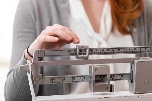 A close-up photo of an unrecognizable woman using a scale in the doctor's office to weigh herself.