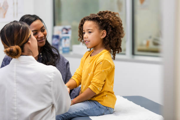 Young female patient talks to her doctor about her symptoms The young female patient smiles while talking to her unrecognizable doctor about her symptoms. girl patient stock pictures, royalty-free photos & images