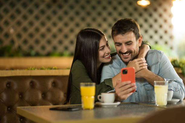 istock Young couple using smart phone and embracing while in a restaurant. 2123116986