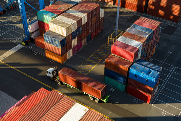 Drone shot of a terminal tractor driving between shipping containers in a massive intermodal container yard in the Port of Long Beach at sunset. \n\nAuthorization was obtained from the Port of Long Beach Security Division and POLB Harbor Patrol for this operation in restricted airspace.