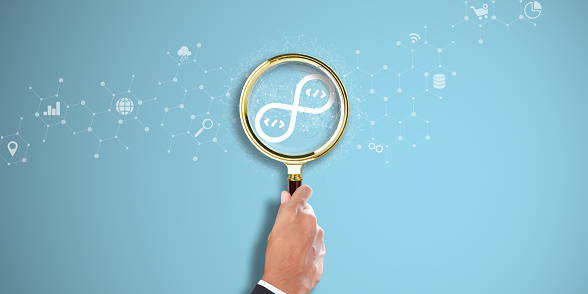 DEVOPS: Businessman Hand holding a magnifying glass with DevOps icon on Light Blue background. Continuous Integration, Continuous Deployment, Agile Development.