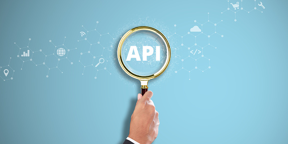 API. Businessman Hand Holding a Magnifying Glass with API Icon on Light Blue Background. Data Integration, Software Connectivity, Application Programming Interface.