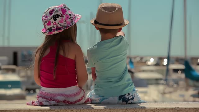 Children are sitting on the stone and looking at the bay with yachts