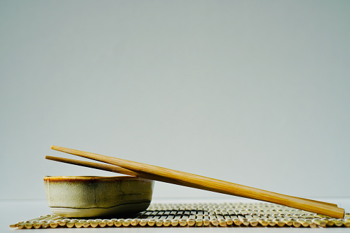 In the image, there are a pair of chopsticks resting on a bamboo sushi rolling mat, next to a small bowl filled with soy sauce. The natural textures of the bamboo and the traditional utensils evoke the essence of Japanese cuisine and the art of sushi making.