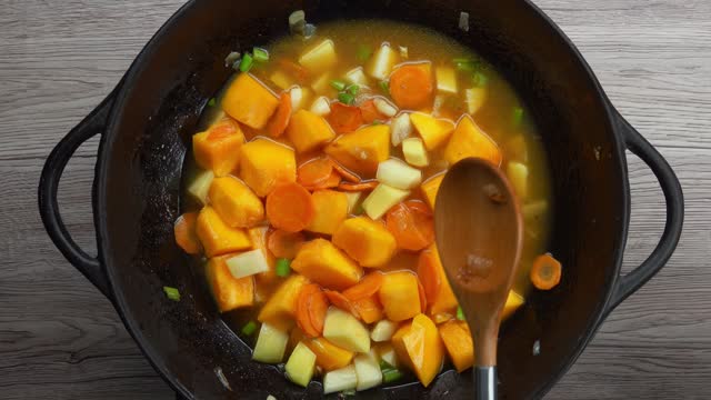 Top view of a wooden spoon stirring pieces of pumpkin with vegetables