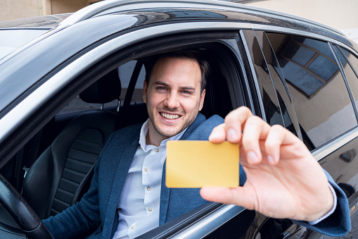 Portrait of an young Caucasian businessman showing an corporate ID card, while passing with an car