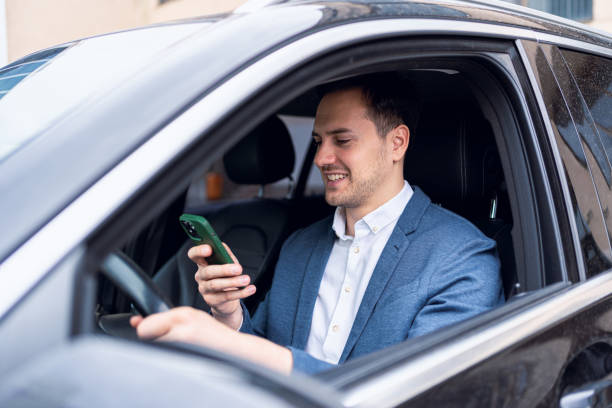 irresponsible caucasian businessman, using mobile phone, while driving the car - mobile phone seat belt text messaging smiling - fotografias e filmes do acervo