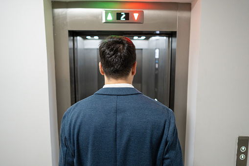 Rear-view of an young Caucasian businessman waiting an elevator