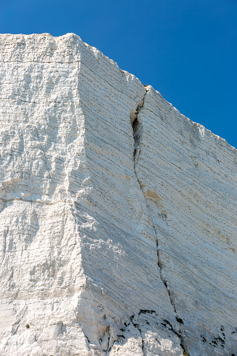 A visible crack in a chalk cliff near Beachy Head, with a blue sky overhead