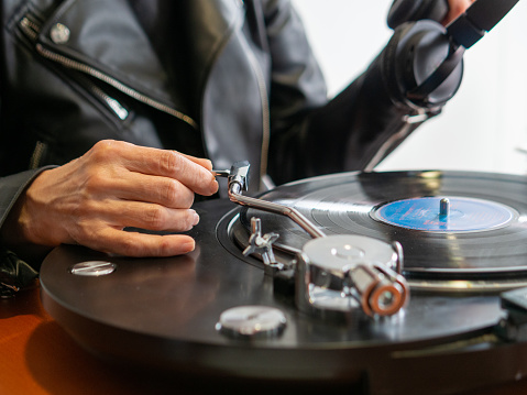 Young woman choosing vinyl disc to play music with turntable on bed, closeup
