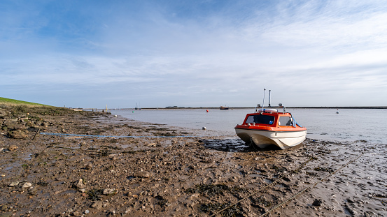 Wells, Norfolk, UK  March 25 2024. Small leisure boat beached on the mud in the estuary at low tide. Captured in the seaside town of Wells on the North Norfolk coast