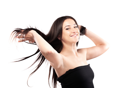 Young woman with long dark hair. Standing confidently in against white background throwing hair in the air.