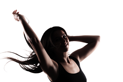 Silhouette of a young woman with long dark hair. Standing confidently in against white background throwing hair in the air.