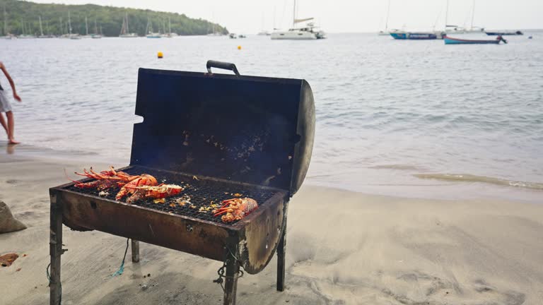 Midsection of Man Cooking Fresh Lobsters on Barbecue Grill at Shore on Beach during Summer