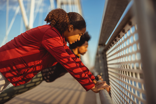 Black teenage daughter with her mother doing push-ups outdoors on the bridge. Living healthy lifestyle. Fitness, sport, people, exercising and lifestyle concept