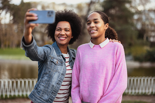 African american mother and teenage daughter taking selfie at the public park. Happy black family having fun outdoors