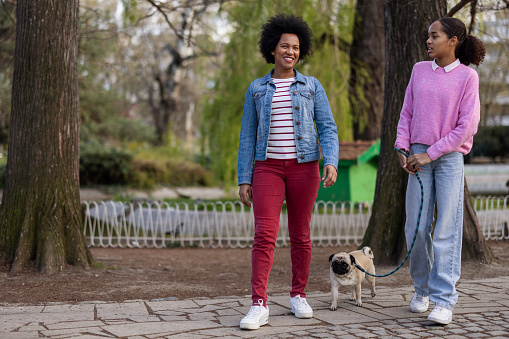 Happy black mother and teenage daughter with their dog having fun outdoors. Enjoying life together