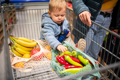 Young mom shopping for fresh and healthy fruits and vegetables for her little boy.