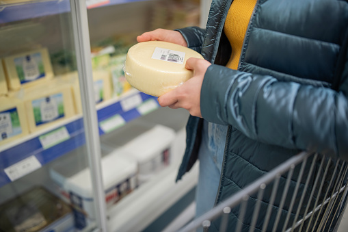 Close-up of a woman looking at block of cheese in the dairy aisle of a supermarket while doing her grocery shopping.