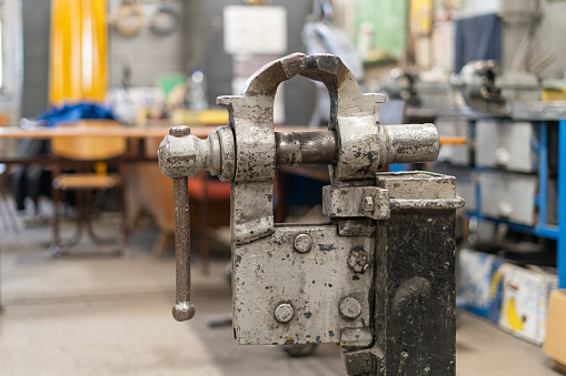 A worn, patinated gray large vise on a rack set up in the middle of an empty welding shop