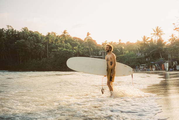 istock Man standing on the beach with surfboard at sunset 2123612114