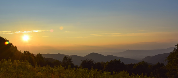 A panorama landscape picture of a sunset in the Shenandoah National Park, during golden hour with the sunrays creating a lens flare; copy space, large size