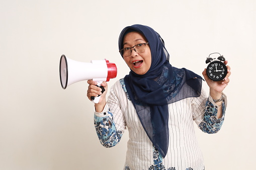 Excited asian elderly woman showing sahur or breaking fast time while shouting using megaphone