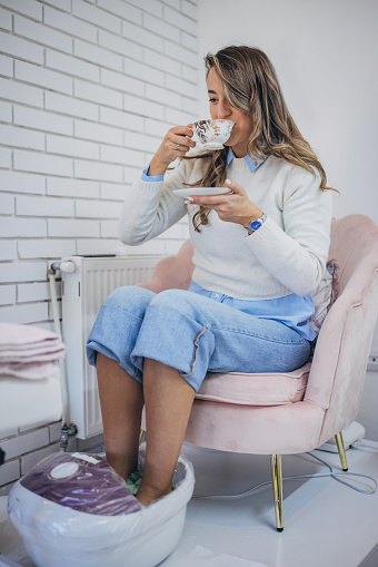 Young lady relishes a hot beverage while getting a pedicure at a modern beauty salon