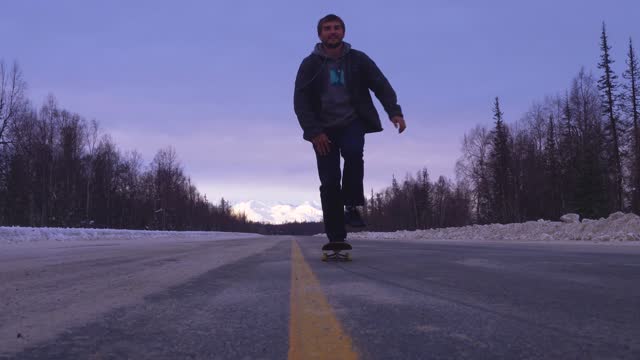 Skater skates through a snowy street with mountan views behind him