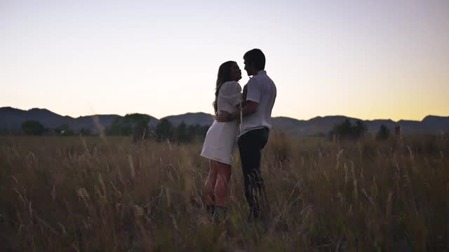 Biy and girl kiss in a field during sunset
