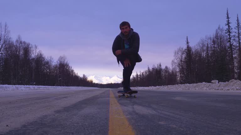 Skater does a trick in a snowy street with mountan views behind him in Alaska