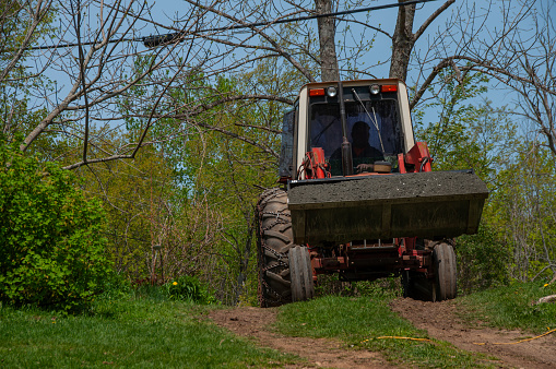 A man driving a red tractor full of gravel in the bucket during spring on a sunny day