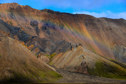 A rainbow at the rugged, multi-coloured rhyolite hills of Vondugil valley, Landmannalaugar, Fjallabak Nature Reserve, Central Highlands, Iceland.