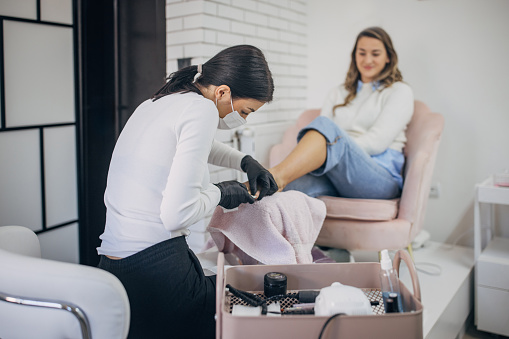 Beautician provides foot care services to a smiling female client in a modern nail salon