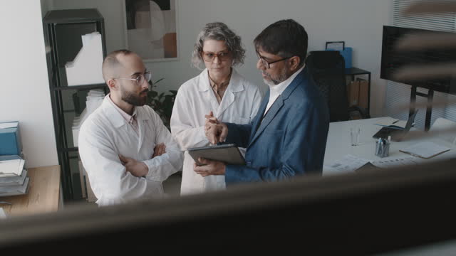 Male Hospital CEO with Tablet and Two Medics Talking in Office
