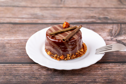 Fresh delicious chocolate cake on plate with fork on wooden background. Caramel glaze and decoration add appeal and desire