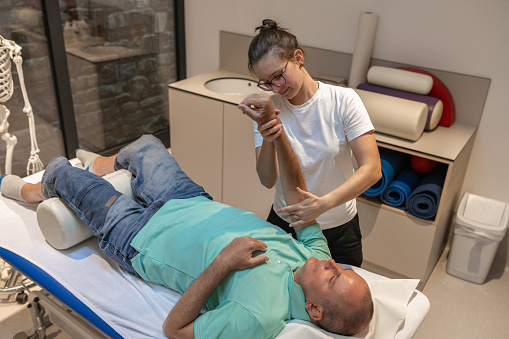 A physiotherapist examines a patient in a wheelchair. A physiotherapist does rehabilitation exercises with a disabled person and a therapy table.