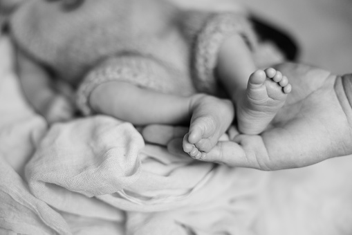 A black and white portrait of a newborn baby sleeping and the parent has his hand around her small feet