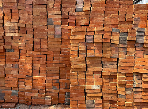 Piles of red bricks stacked on top of one another. Red bricks are common building wall materials at construction site.