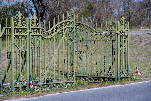 Chincoteague Island, Virginia, USA - March 21, 2024: A well-weathered, ornate wrought iron gate and fence surrounding a historic cemetery in the Town of Chincoteague.