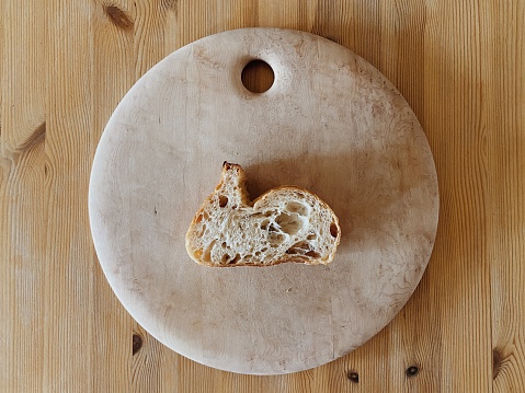 Sliced Italian Batard bread that looks like an Easter bunny on a round wooden cutting board on a wooden table background.