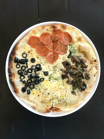 Classic baked italian pizza with pepperoni, mushrooms, mozarella cheese, and black olives served on dark black wooden rustic table.