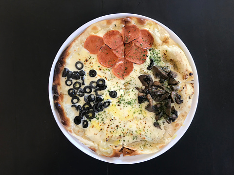 Classic baked italian pizza with pepperoni, mushrooms, mozarella cheese, and black olives served on dark black wooden rustic table.