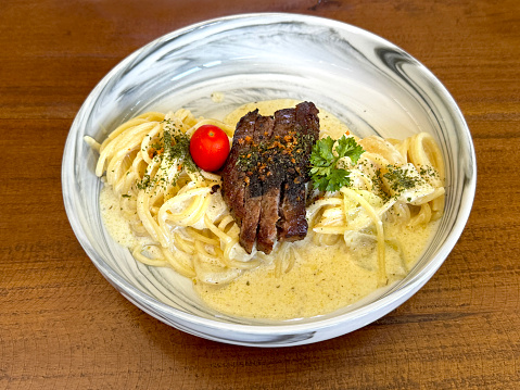 Pasta spaghetti carbonara with baby tomatoes and grilled beef slices. served on a wooden table.