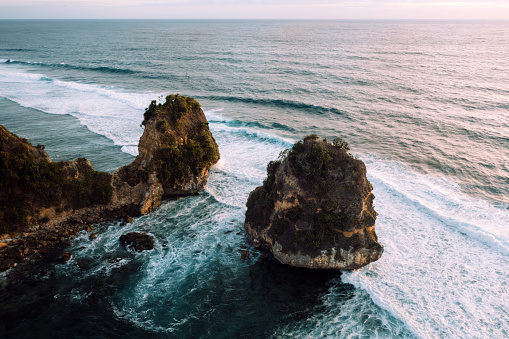Sumba Island Indonesia, Sunset twilight over natural Sumba Nihisumba Beach with coastal twin rock formation. Waves from the Indian Ocean splashing towards the natural exotic beach under beautiful sunset twilight at dusk. Aerial Drone Point of View. Sumba Island, Nusa Tenggara Timur, Indonesia, Southeast Asia