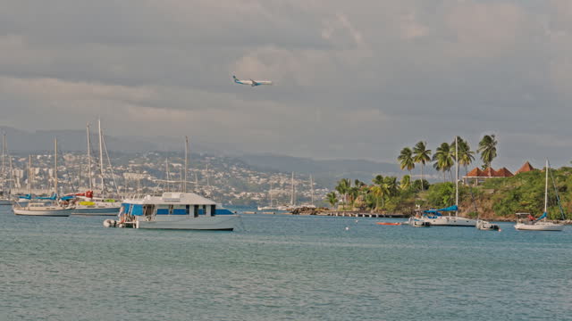 Airplane Flying Under Yachts Sailing on Sea at Caribbean Island