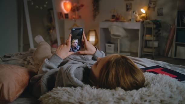 istock Girl talks with brother by video chat using phone lying on bed at home 2124265972