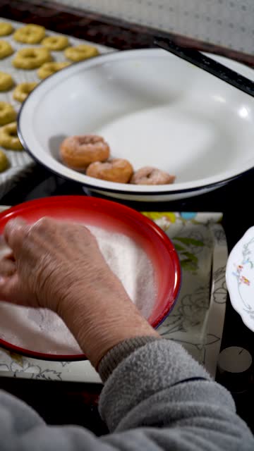 A person covers homemade donuts with sugar.