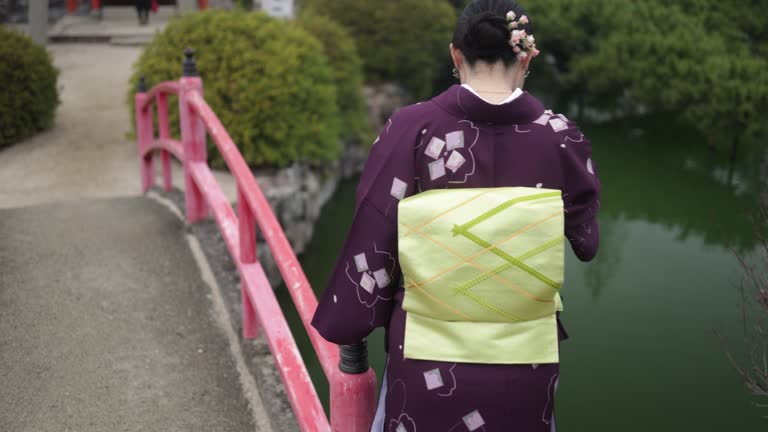 Woman in kimono looking at carps in pond in temple - slow motion